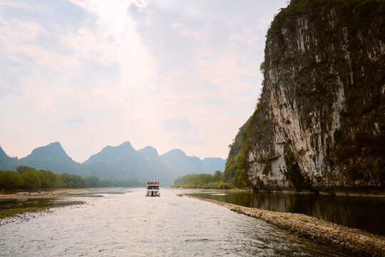A boat travels along a river surrounded by towering limestone cliffs and lush greenery. Li River, Li Jiang, Guangxi, China