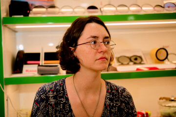 Woman with glasses and dark hair standing in a shop with glasses displayed on shelves. Guangzhou, Guangdong, China