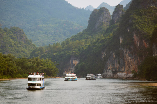 Boats navigate a serene river surrounded by lush green mountains under a cloudy sky. Li River, Li Jiang, Guangxi, China