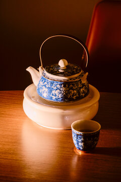 Blue and white ornate teapot with a teacup on a wooden table lit warmly. Guangzhou, Guangdong, China