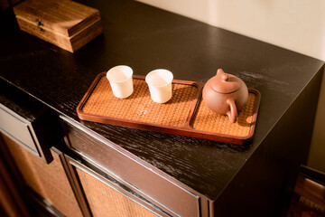 Wooden tray with brown teapot and two white cups on dark cabinet surface, warm lighting. Trip from Guilin to Chengdu, Guangxi, Sichuan, China
