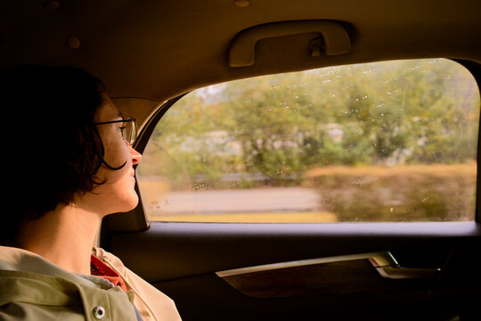 Woman with short hair and glasses gazes out a car window at a blurred landscape. Trip from Guilin to Chengdu, Guangxi, Sichuan, China