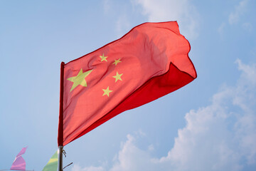 Chinese flag waving against a clear blue sky with white clouds in the background. Trip from Guilin to Chengdu, Guangxi, Sichuan, China