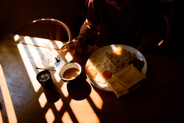 Sunlit breakfast scene with eggs, toast, coffee, and a person using a phone at a table. Trip from Guilin to Chengdu, Guangxi, Sichuan, China