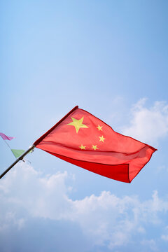 Chinese flag waving against a bright blue sky with soft white clouds. Trip from Guilin to Chengdu, Guangxi, Sichuan, China