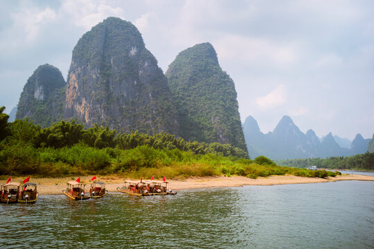 Traditional wooden boats with red flags on a river in front of karst mountains and lush greenery. Trip from Guilin to Chengdu, Guangxi, Sichuan, China