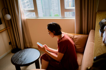 Person in a red outfit sits on a sofa using a smartphone in a modern apartment. Hongkong, China