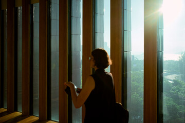 Woman looking out tall windows as sunlight streams in. Hongkong, China