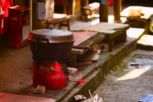 Large black pot on a traditional outdoor clay stove in a rustic setting, sunlight filtering through. Longji (Longsheng) Rice Terraces, Longsheng, China