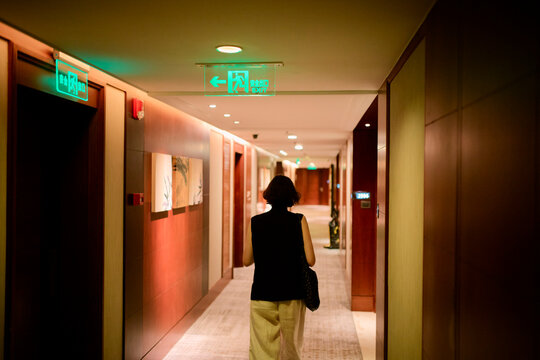 Woman walking through a hotel corridor with dim lighting and emergency exit signs. Shanghai, China