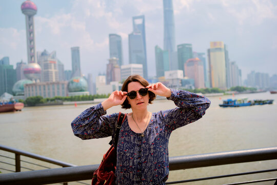 Woman adjusting sunglasses with modern city skyline and river in the background. Shanghai, China