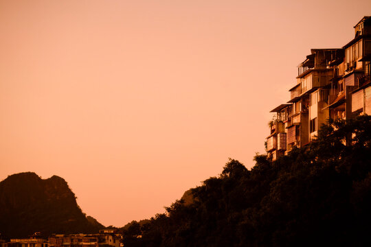 Cliffside houses with a warm sunset backdrop create a serene, picturesque landscape scene. Longji (Longsheng) Rice Terraces, Longsheng, China