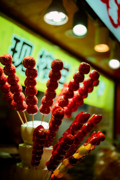 Candied fruit skewers brightly displayed at a street food market stall under colorful lights. Shanghai, China