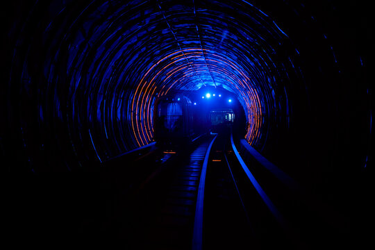 A train travels through a dimly lit tunnel with vibrant blue and orange lights. Shanghai, China
