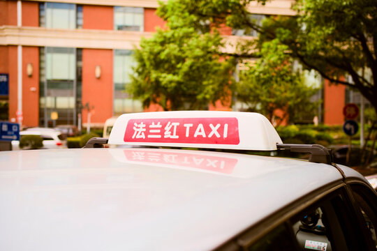Close-up of taxi sign on a car roof with a building and trees in the background. Shanghai, China