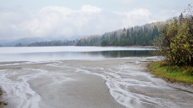 Serene lake landscape with sandy shore, distant forest, and overcast sky. Thunder Bay, Ontario, Canada