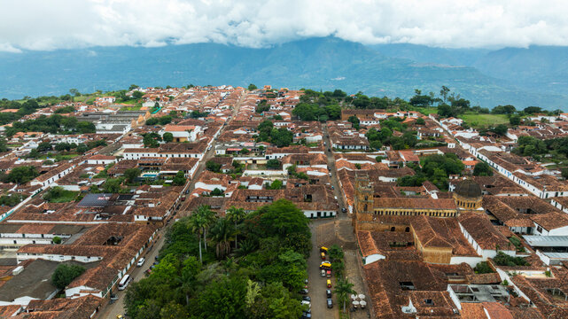 Aerial view of a historic town with red-tiled roofs and lush greenery under a cloudy sky. Barichara, Colombia