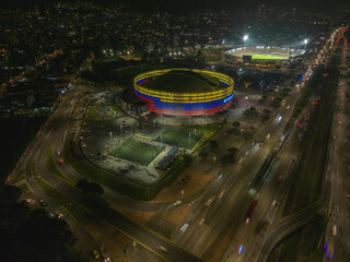 Night aerial view of a brightly lit stadium and bustling city traffic. Bogota DC, Colombia