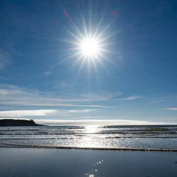 Bright sun over a serene ocean beach with clear blue skies and gentle waves. Tofino, British Columbia, Canada