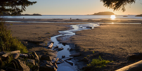 Sunset over a serene beach with a winding stream and distant islands. Tofino, British Columbia, Canada