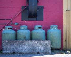 Four large green gas cylinders lined up against a red brick wall with pipes and a vent. Tofino, British Columbia, Canada