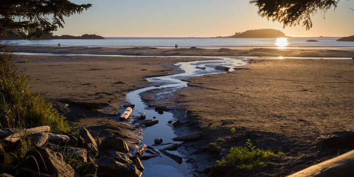 Sunset over a serene beach with a winding stream and distant islands. Tofino, British Columbia, Canada