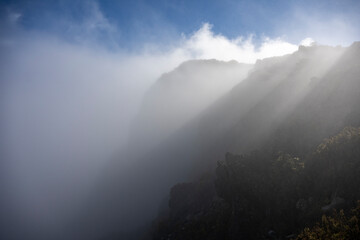 Misty mountain slope with sunlight breaking through clouds against a blue sky. Kula, Hawaii, USA