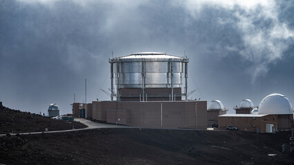Observatory domes sit against a dramatic cloudy sky on a rocky landscape. Kula, Hawaii, USA