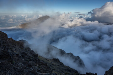 Dramatic mountain peaks piercing through a sea of clouds under a vivid blue sky. Kula, Hawaii, USA