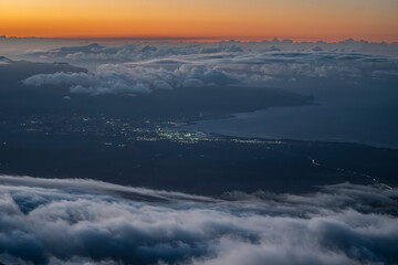 Aerial view of a mountainous coast at sunset with clouds and city lights below. Kula, Hawaii, USA