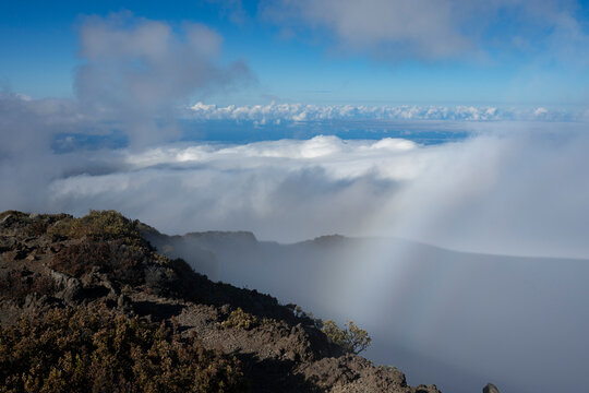 Mountain landscape above clouds with sunlight creating a subtle rainbow effect in the sky. Kula, Hawaii, USA