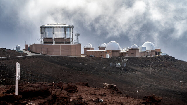 Observatory complex with telescopes under a cloudy sky on a rocky, barren landscape. Kula, Hawaii, USA
