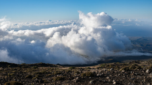 Expansive view of fluffy clouds over rugged mountain terrain under a clear blue sky. Kula, Hawaii, USA