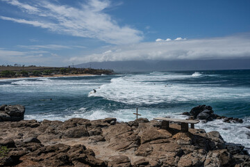 Rocky coastline with ocean waves crashing under a clear blue sky with scattered clouds. Haiku, Hawaii, USA