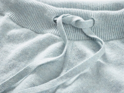 Close-up of a light blue sweatshirt with a tied drawstring on a ribbed waistband.