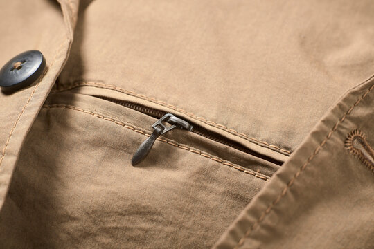 Close-up of a tan fabric zipper on a stitched pocket with a black button nearby.