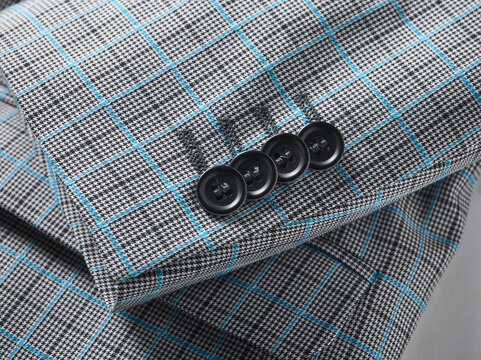 Close-up of a gray checkered suit sleeve with blue lines and black buttons.