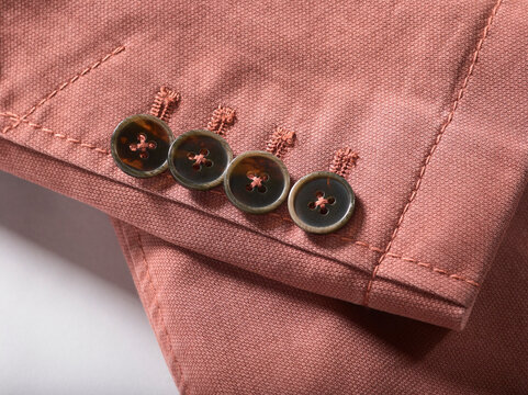 Close-up of a pink fabric blazer sleeve with four dark buttons in a row
