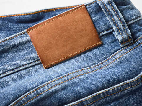 Close-up of blue denim jeans with brown leather patch, highlighting texture and stitching.