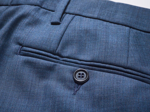 Close-up of elegant blue trousers pocket with button detail, showcasing fine fabric texture.