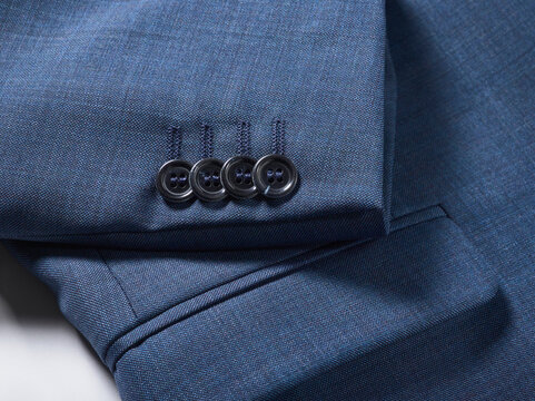 Close-up of a navy blue suit sleeve with four black buttons on a white surface.