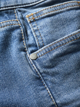 Close-up of blue denim jeans fabric with a visible pocket and stitching details.