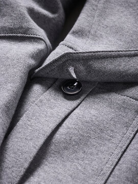 Close-up of a button on a grey textured fabric with distinct stitching.