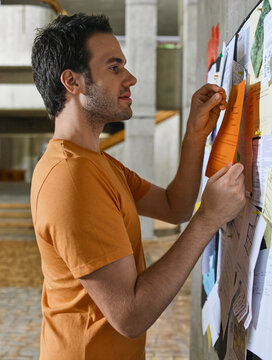 Young man posting a notice on a bulletin board in a modern building hallway. Germany