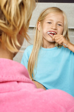 Child brushing teeth happily while looking over shoulder at adult indoors. Germany