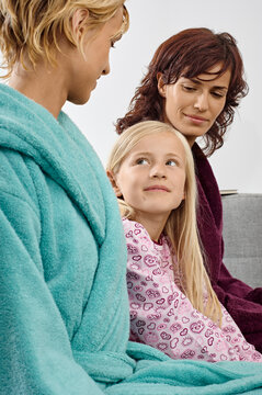 Three women in bathrobes smiling and seated on a couch at home. Germany