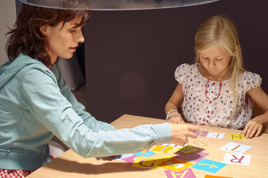 Woman and child playing with colorful alphabet flashcards at a wooden table. Germany