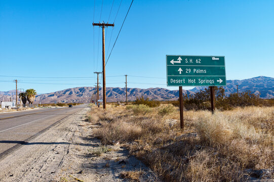 Roadside in desert with sign pointing to 29 Palms and Desert Hot Springs under clear sky. USA