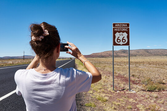 Woman taking a photo of Arizona US 66 road sign on a sunny day in a vast landscape. USA