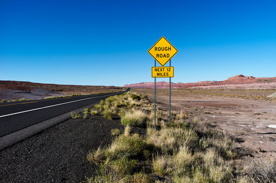 Desert road with rough road sign and distant red cliffs under a clear blue sky.  USA
